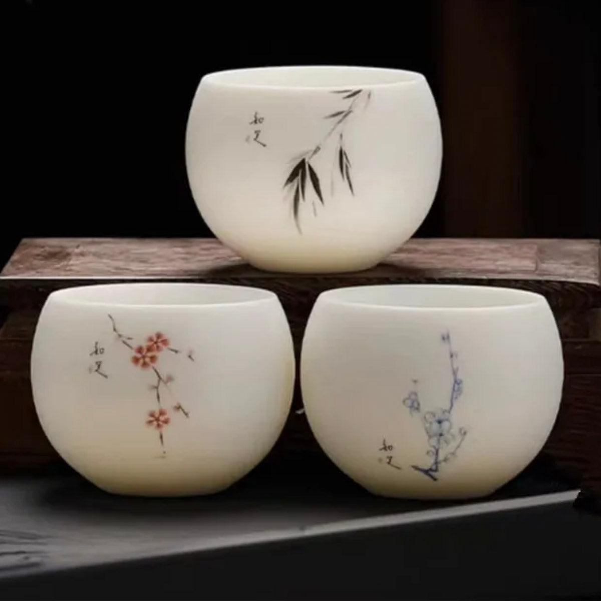Three white ceramic cups with floral and leaf designs on a dark background