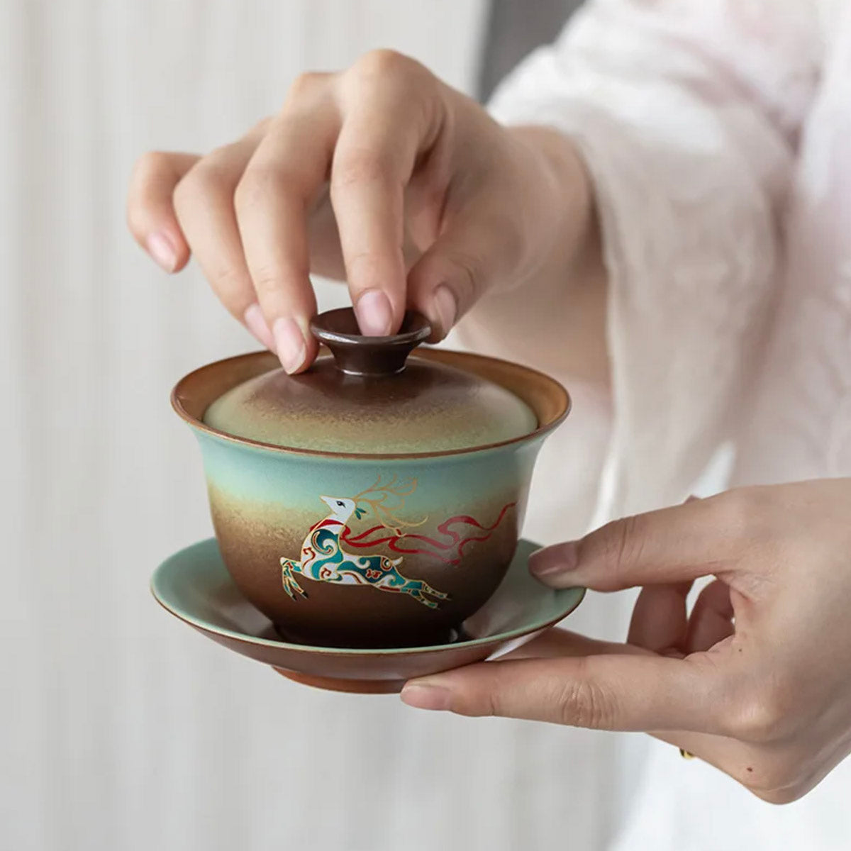 Person holding a traditional ceramic teapot with artistic design on a plain background