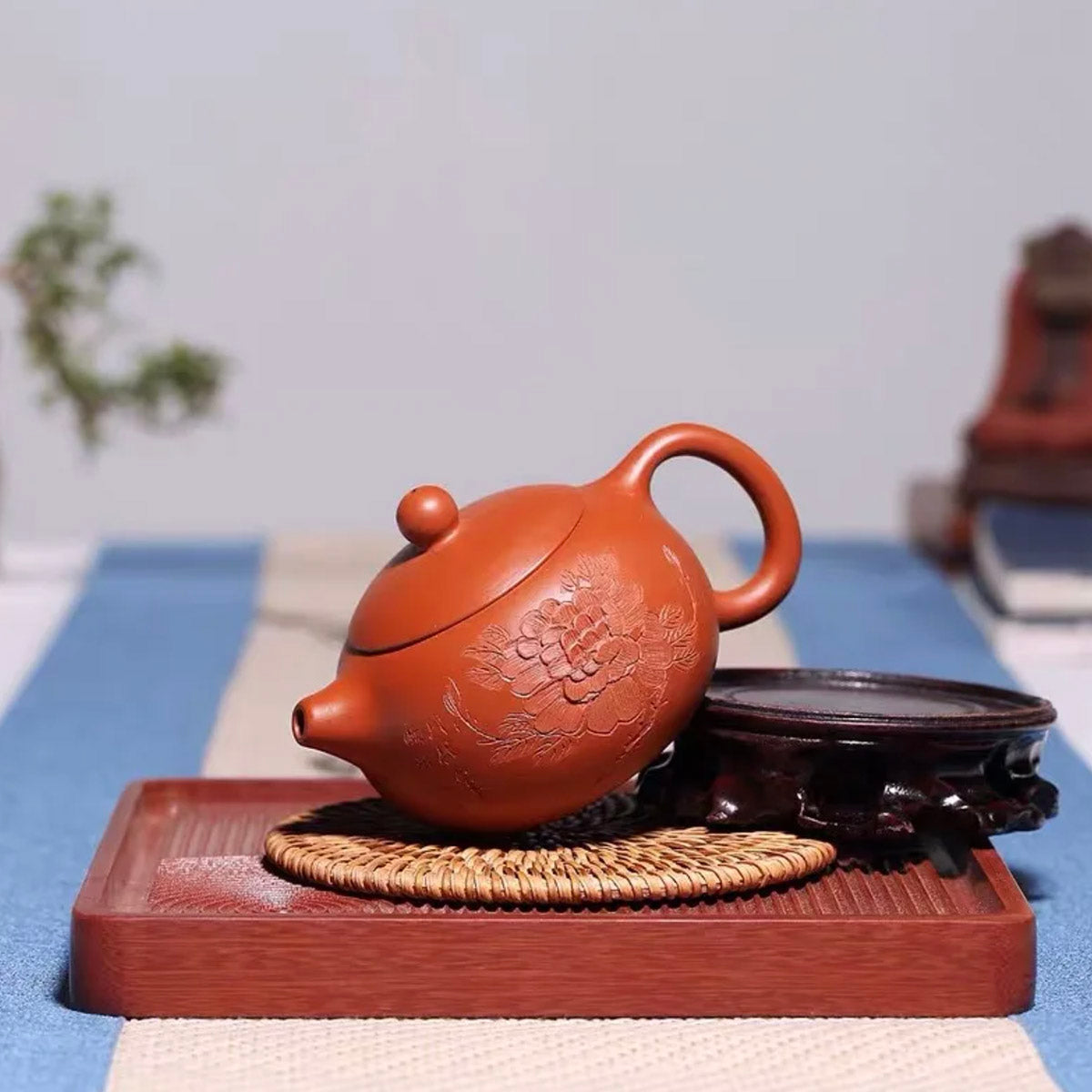 Red clay teapot on a wooden tray with a blurred background