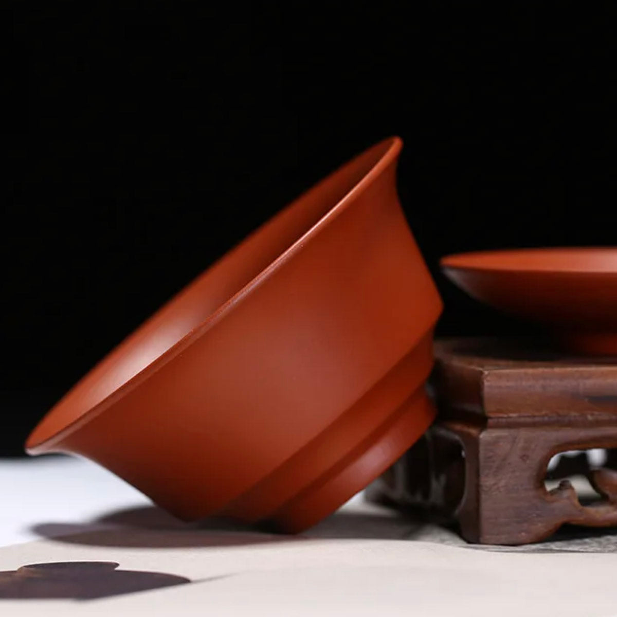 Red ceramic bowl on a wooden stand with a dark background