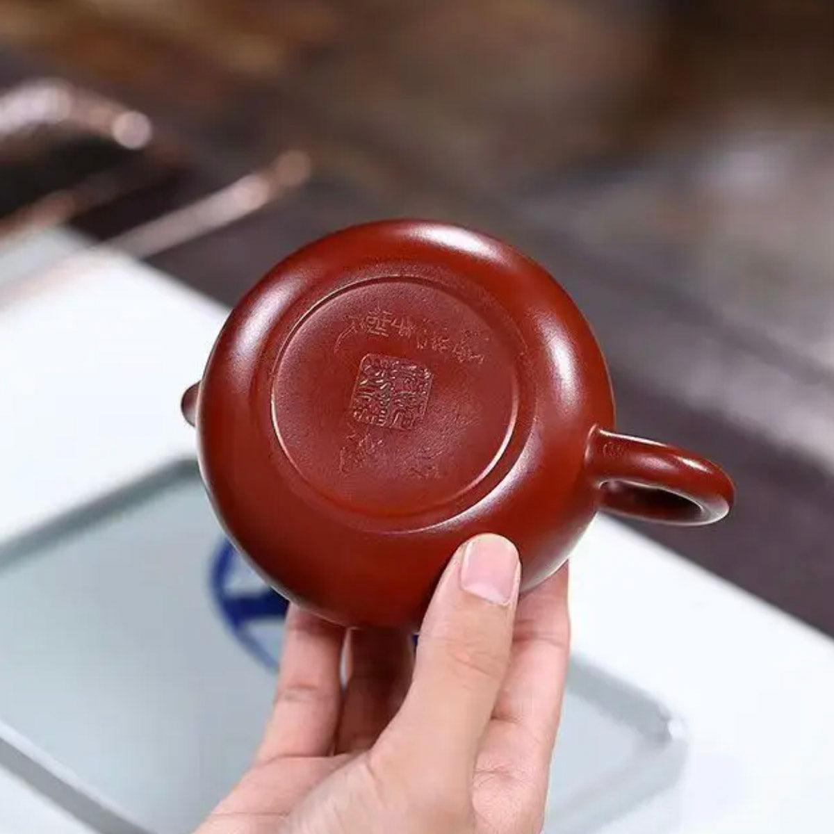 Red ceramic teapot held by a hand with a blurred background