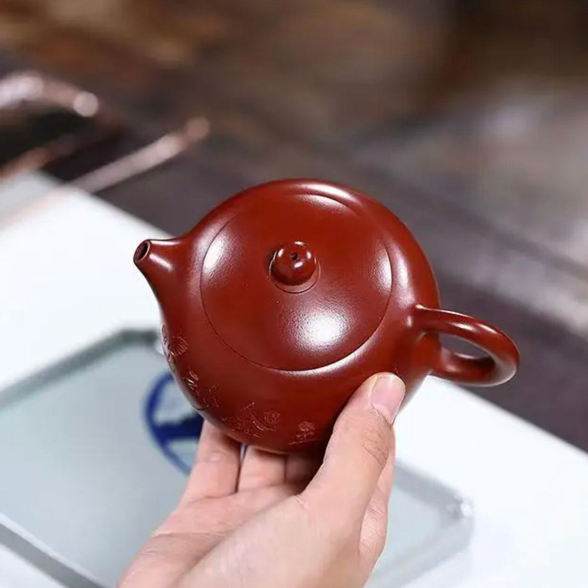 Red teapot held in a hand with a blurred background
