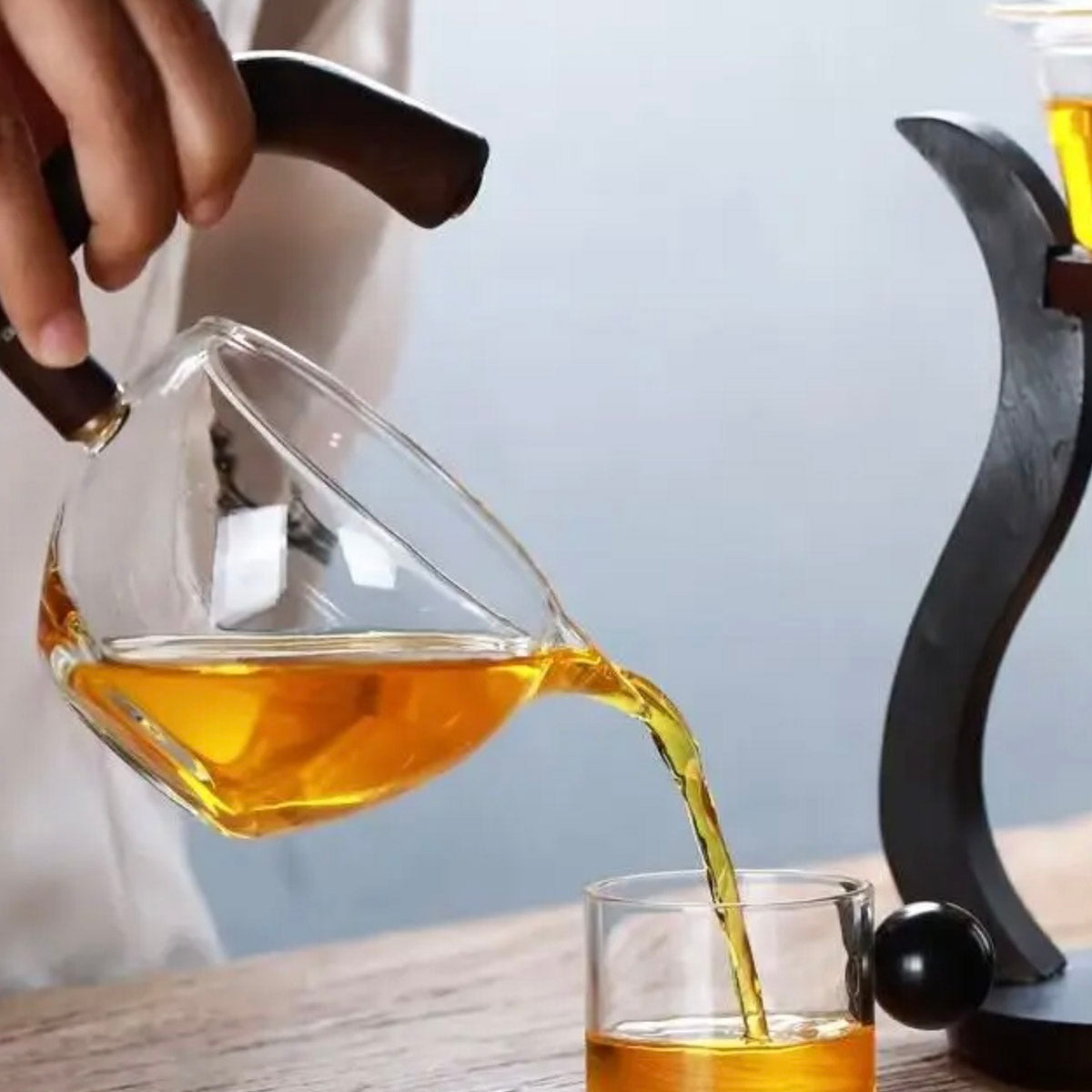 Glass teapot being filled with tea into a glass cup on a wooden surface.