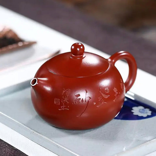 Red ceramic teapot with Chinese characters on a white tray